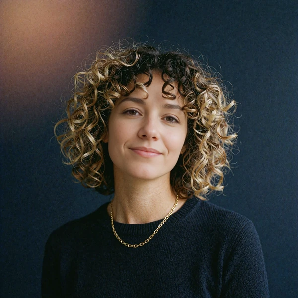 Portrait of a woman with voluminous curly hair smiling gently, representing an illustrative community voice
